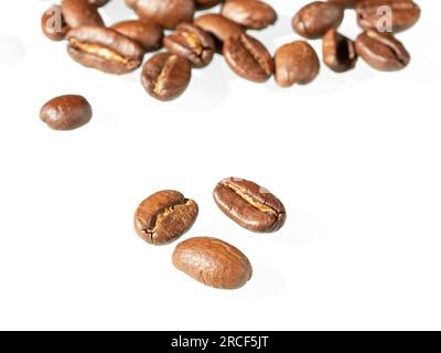 Trois grains de café torréfiés au premier plan et un bouquet de grains de café en arrière-plan sur fond blanc Banque D'Images