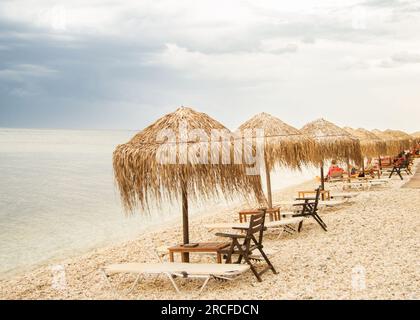 Magnifique plage paysagée en Grèce avec parasols en paille et chaises longues rouges très proche de l'eau bleue Banque D'Images