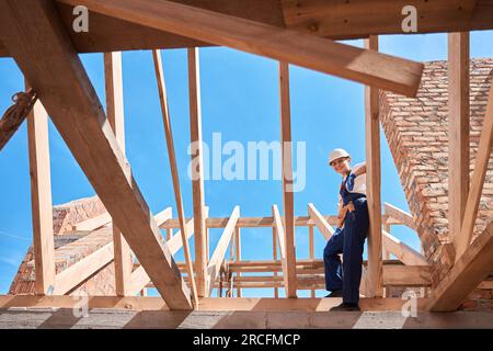 Femme ingénieur du bâtiment debout sur la poutre en bois du cadre de toit Banque D'Images