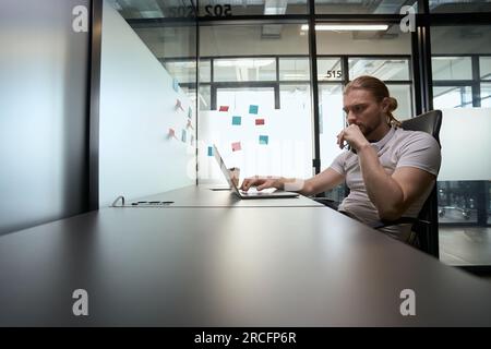 Homme attentionné assis à son bureau devant l'ordinateur portable Banque D'Images
