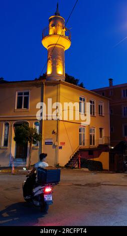 Livreur sur une moto la nuit dans une rue d'Istanbul Turquie avec un bâtiment et un minaret derrière. Banque D'Images