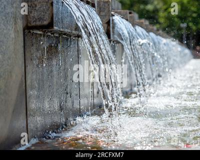 L'eau coule sur les dalles de pierre de la fontaine de la ville. Fontaine dans le parc de la ville. Banque D'Images