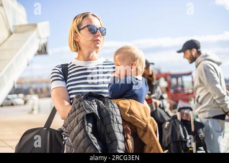 Motherat voyageant avec son bébé garçon enfant. Maman tenant son sac de voyage et son bébé garçon enfant tout en faisant la queue pour le bus devant la gare de l'aéroport Banque D'Images