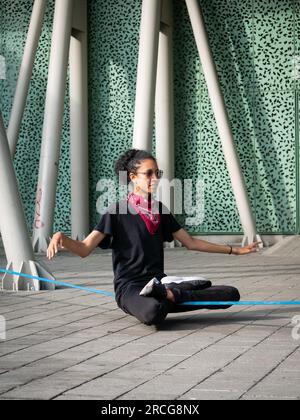 Femme colombienne portant un pantalon noir et un T-shirt est assise sur une corde bleue pratiquant Slack Line Banque D'Images