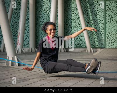 Femme colombienne portant un pantalon noir et un T-shirt est assise sur une corde bleue pratiquant Slack Line Banque D'Images