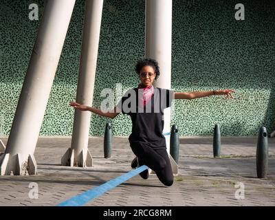 Femme colombienne portant un pantalon noir et un T-shirt est assise sur une corde bleue pratiquant Slack Line Banque D'Images