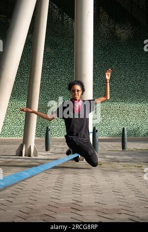 Femme colombienne portant un pantalon noir et un T-shirt est assise sur une corde bleue pratiquant Slack Line Banque D'Images