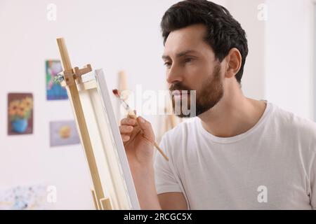 Homme peinture en studio. Utilisation du chevalet pour tenir la toile Banque D'Images