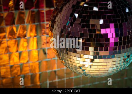 Boule disco brillante contre rideau de fête en aluminium sous la lumière orange. Espace pour le texte Banque D'Images