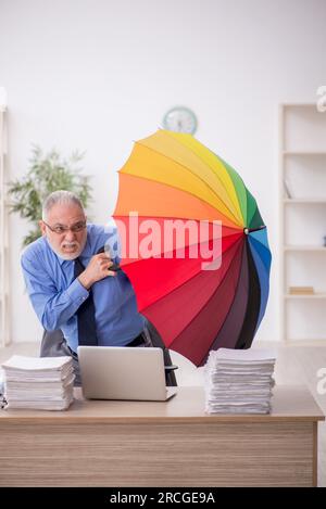 Ancien employé tenant un parapluie sur le lieu de travail Banque D'Images