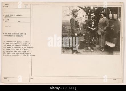 Mlle Tsiania de l'Oklahoma et Mme Hunt de la Y.M.C.A. sont photographiées aux côtés du major John A. Lejeune, commandant de la deuxième division américaine de l'armée d'occupation en Allemagne. La tête indienne à l'intérieur d'une étoile sert de marque d'identification pour la division. Banque D'Images