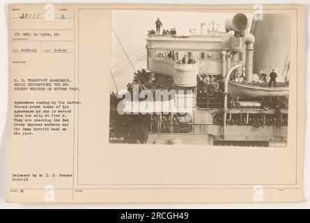 Géo. Lt. H. Lyon a capturé une image des États-Unis Transport Agamemnon revenant d'un voyage par temps violent pendant la première Guerre mondiale. La photographie montre des troupes rassemblées sur le pont de l'Agamemnon alors qu'il est amené dans le quai 4, où ils acclament les travailleurs de la Croix-Rouge cantine et la bande du Camp Merritt. Publié par le M.I.D. Censurer le 19 février 1919. Banque D'Images