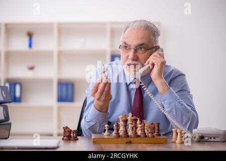 Un vieil employé de sexe masculin joue aux échecs dans le bureau Banque D'Images