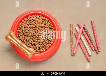 Bol avec de la nourriture sèche pour chien et des friandises sur fond de couleur Banque D'Images