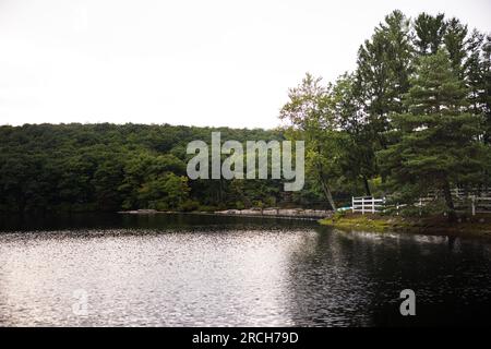 Un paysage avec une propriété au bord du lac entourée de forêts conduisant sur la route avec un arc-en-ciel à la fin et des gouttes de pluie sur le rebord de la fenêtre. Banque D'Images