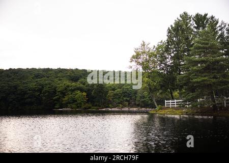 Un paysage avec une propriété au bord du lac entourée de forêts conduisant sur la route avec un arc-en-ciel à la fin et des gouttes de pluie sur le rebord de la fenêtre. Banque D'Images