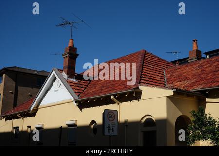 Le toit à pignon en tuiles rouges d'une fédération sur Bondi Road, mur latéral jaune à l'ombre profonde contre un ciel bleu profond Bondi, Nouvelle-Galles du Sud Banque D'Images