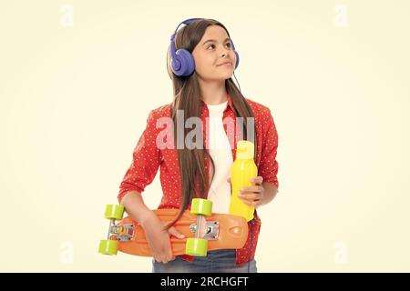 Jeune fille d'école avec bouteille d'eau de planche à roulettes et casque sur fond isolé de studio. Printemps écofille tendance, urbain style adolescent. Banque D'Images