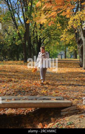 La photo a été prise dans le parc d'Odessa appelé le jardin Dyukovsky. Sur la photo, une jeune femme marche dans le parc d'automne, bottant des feuilles couchées sur le Banque D'Images