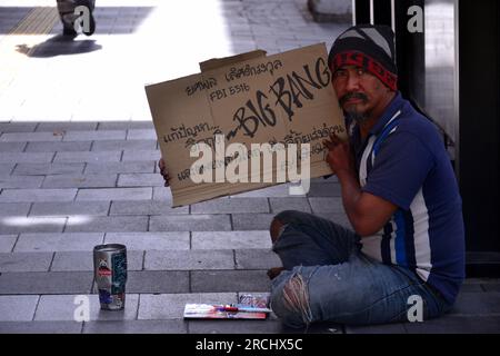 Un homme est assis sur un trottoir dans le centre de Bangkok, Thaïlande, Asie, tenant une pancarte qui dit : «BIG BANG» avec un texte en langue thaïlandaise qui exprime sa préoccupation pour l'avenir de la terre. En face de lui se trouve une tasse pour inviter des dons. Banque D'Images