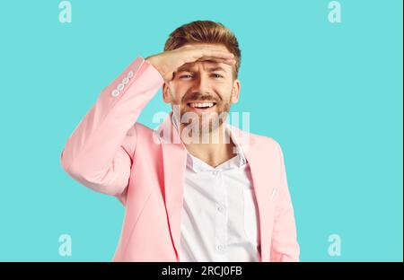 Heureux jeune homme en costume rose tient sa main sur le front au-dessus des yeux et regarde au loin Banque D'Images