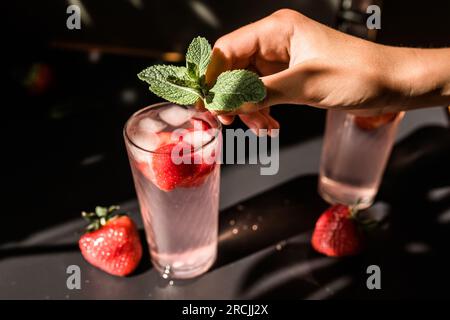 Barista main mettant des feuilles de menthe fraîche sur un cocktail de fraises et de lymyon. Thé glacé fraise-myrtille. Un modèle coloré et revigorant Banque D'Images