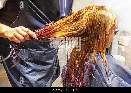 séchez les cheveux longs et humides de couleur vive des enfants en lilas et rose clair avec un sèche-cheveux Banque D'Images