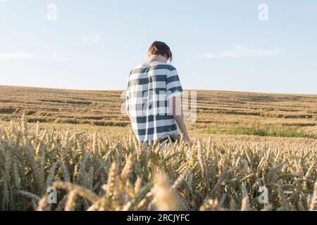 Un jeune garçon, un adolescent avec des oreilles de blé mûr dans un champ de fermier, contre un ciel bleu. Grain pour faire du pain. le concept de crise économique et hu Banque D'Images