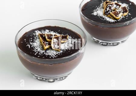 Pudding au cacao, noix de coco décorée, dans des bols en verre, sur surface blanche Banque D'Images