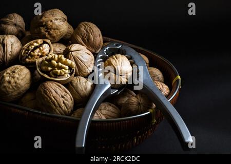 Noix nouvellement récoltées, conçues dans un panier en osier, avec un craquelin de noix, sur une surface noire Banque D'Images