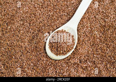 Graines de lin sèches et naturelles dans une cuillère en bois, sur des graines de lin entassées, vue de dessus Banque D'Images