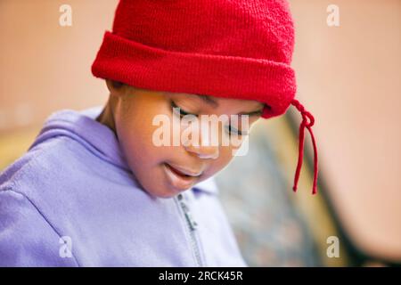 portrait d'une fille africaine de village avec bonnet rouge situé sur le banc en face de la maison Banque D'Images