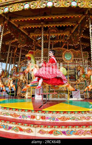 Femme en robe d'époque chevauchant un carrousel classique, Merry Go Round, à l'événement vintage Goodwood Revival 2011. Manège rond-point Banque D'Images