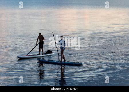 Femme et jeune garçon sur paddle board au coucher du soleil dans le lac. Golden Lake Ontario Canada Banque D'Images