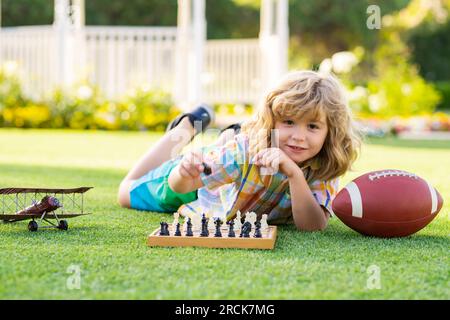 Enfant jouant au jeu d'échecs dans l'arrière-cour du printemps, en posant sur l'herbe. Jeu d'échecs concentré. Enfant jouant à un jeu de société en extérieur. Banque D'Images