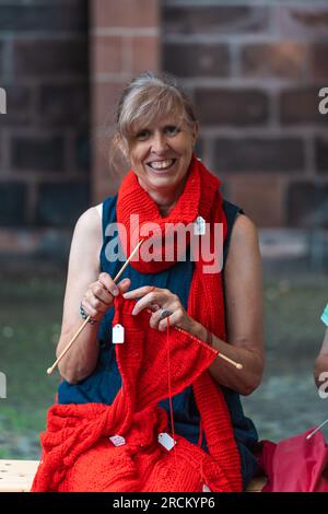 Kaiserslautern, Allemagne. 15 juillet 2023. Enchantée spectateur féminin tricotant une longue écharpe rouge. Trois jours de spectacles de rue théâtraux et de musique offerts par 200 artistes internationaux dans le centre-ville de Kaiserslautern - jour 2. Crédit : Gustav Zygmund/Alamy News Banque D'Images