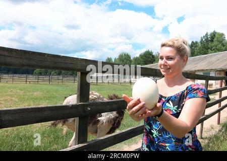 Une femme tient un œuf d'autruche dans ses mains. Autruches dans un zoo pour enfants. Dans une cage en bois. Banque D'Images