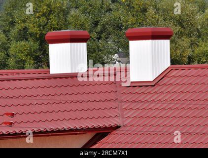 Une cheminée sur le toit d'une maison recouverte de tuiles métalliques ou d'un profilé métallique Banque D'Images