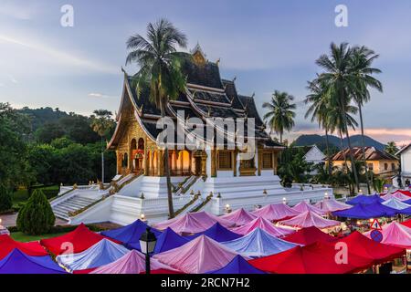 Temple Wat Ho Pha Bang situé dans le parc de l'ancien palais royal du Laos aujourd'hui musée. Des tentes roses, bleues et rouges peuplent la rue en face. Banque D'Images