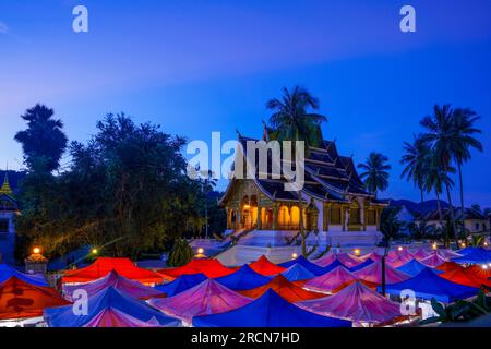 Temple Wat Ho Pha Bang situé dans le parc de l'ancien palais royal du Laos aujourd'hui musée. Des tentes roses, bleues et rouges peuplent la rue en face. Banque D'Images