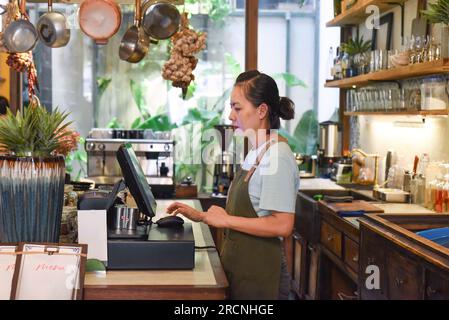 Jeune serveuse vietnamienne travaillant avec la machine de check out dans le café Banque D'Images