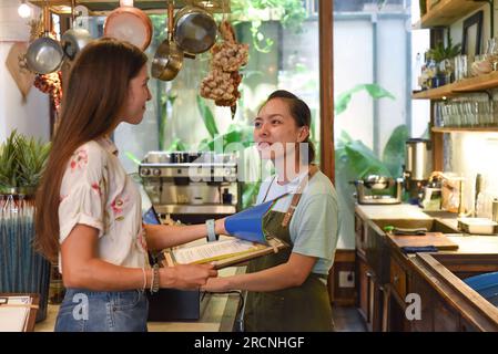 Jeune serveuse vietnamienne travaillant avec la machine de check out et les clients dans le café Banque D'Images