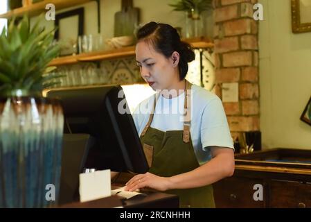 Jeune serveuse vietnamienne travaillant avec la machine de check out dans le café Banque D'Images