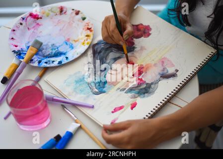 Femme peignant dessin à l'aquarelle de fille asiatique avec pinceau sur une table avec de l'eau et des peintures Banque D'Images
