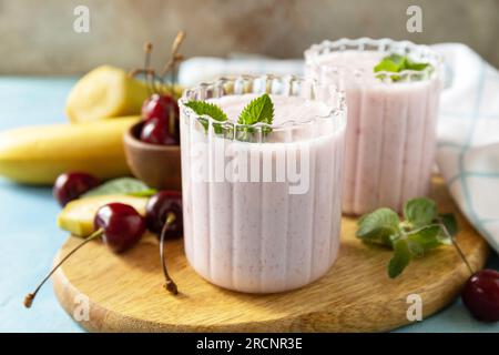 Smoothies à la cerise douce et banane avec du yaourt sur une planche de bois sur un fond de pierre. Smoothies frais de saison. Banque D'Images