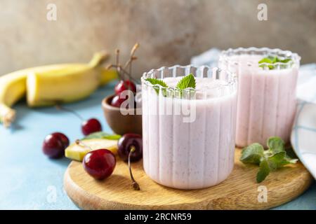 Smoothies frais de saison. Smoothies à la cerise douce et banane avec du yaourt sur une planche de bois sur un fond de pierre. Banque D'Images