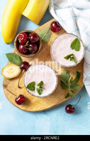 Smoothies à la cerise douce et banane avec du yaourt sur une planche de bois sur un fond de pierre. Smoothies frais de saison. Vue d'en haut. Espace de copie. Banque D'Images