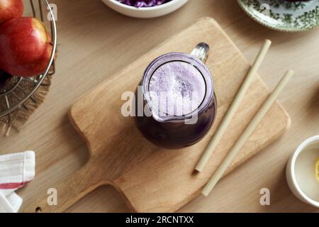 Jus de chou violet dans une cruche en verre avec des pommes fraîches et des pailles de bambou Banque D'Images