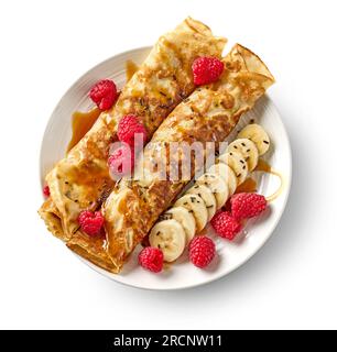 crêpes fraîchement cuites avec des fruits frais et sauce caramel sur plaque blanche isolée sur fond blanc, vue de dessus Banque D'Images