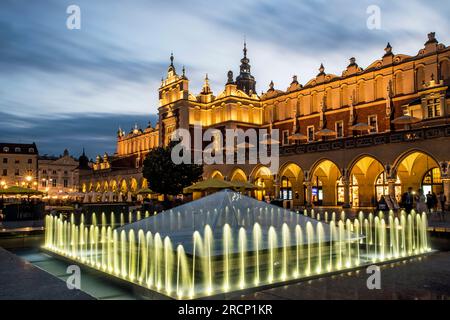 La place du marché et la salle aux tissus dans le centre de Cracovie, en Pologne, le soir avec des jets d'eau allumés pour encourager les visiteurs à venir regarder Banque D'Images